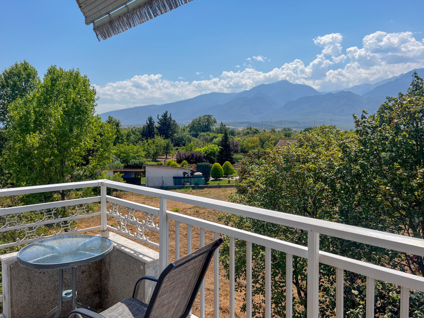 Balcony with a small table and chairs, offering a scenic view of mountains and surrounding greenery.