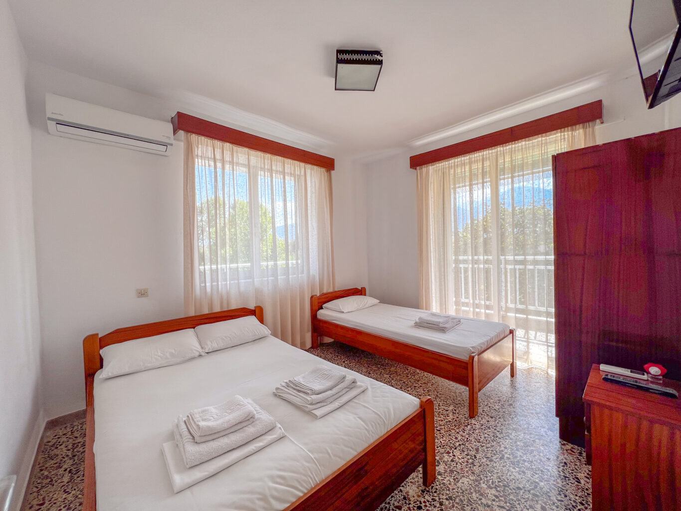 Spacious hotel room with a double bed, a single bed, large windows, and natural light filling the room