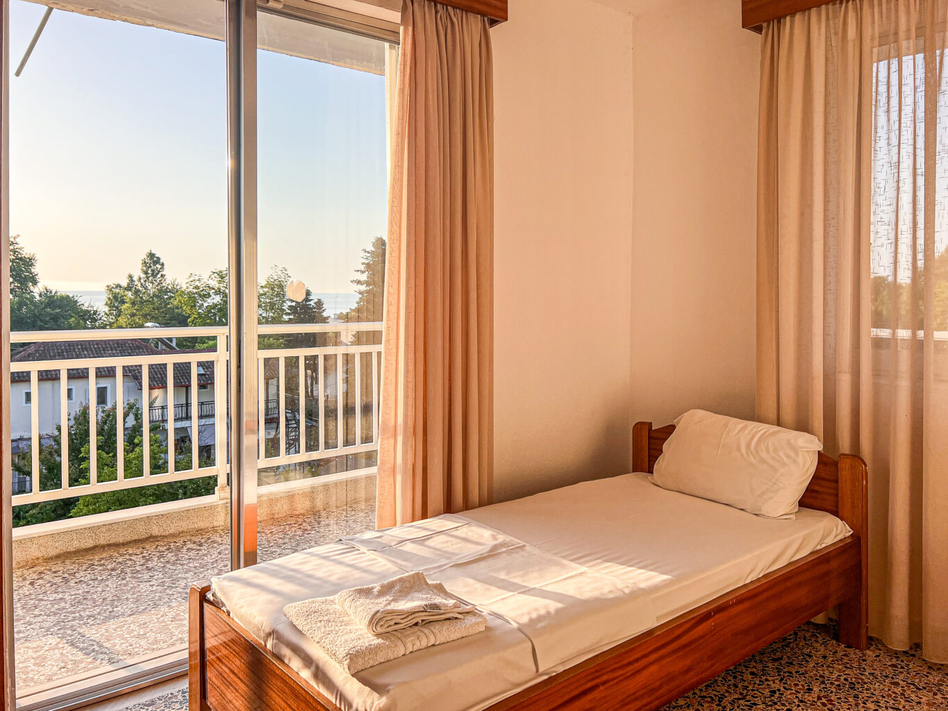 Bright room with a single bed, large windows, and a view of the sea from the balcony