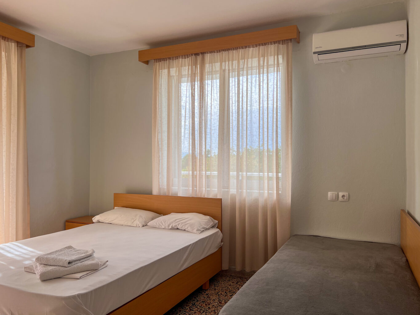 Bright hotel room with a double bed and a single bed, featuring large windows and natural light