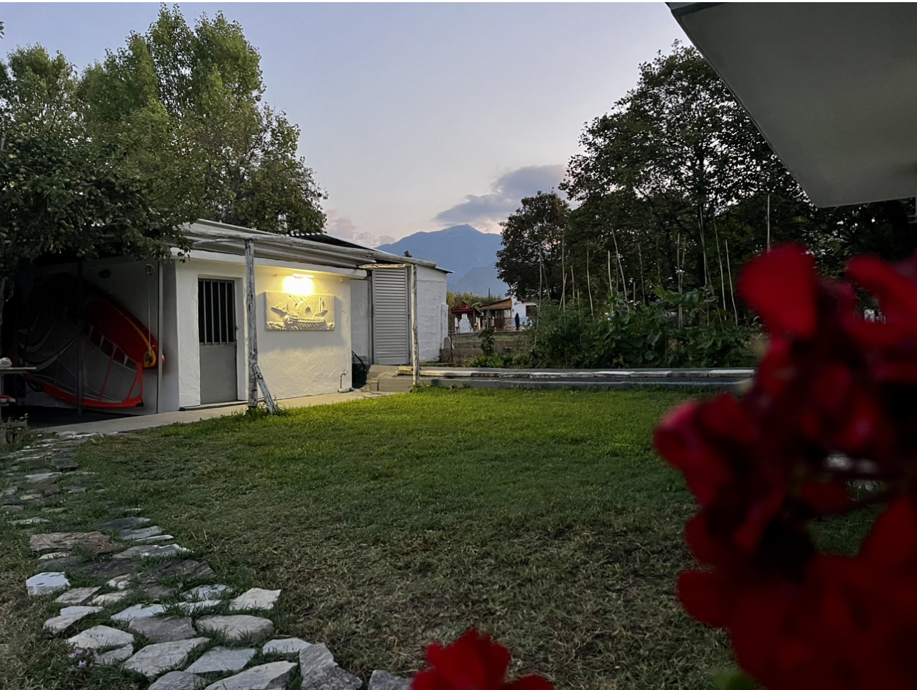 Small garden house with lighting at dusk, surrounded by greenery and a view of Mount Olympus in the background.