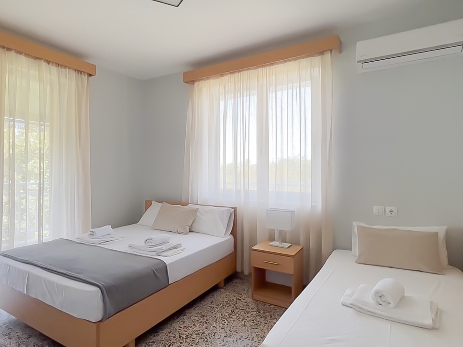 Bright and cozy hotel room with a double bed and a single bed, featuring large windows and natural light