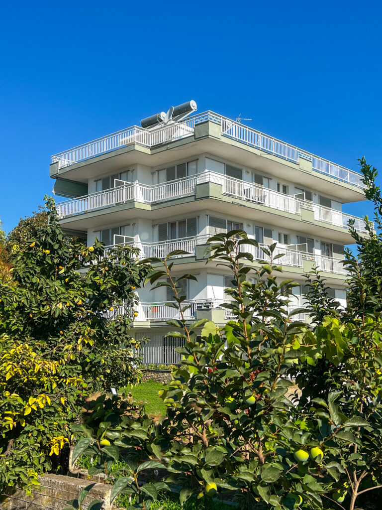 View of Prado Hotel building with solar panels on the roof, surrounded by greenery and trees