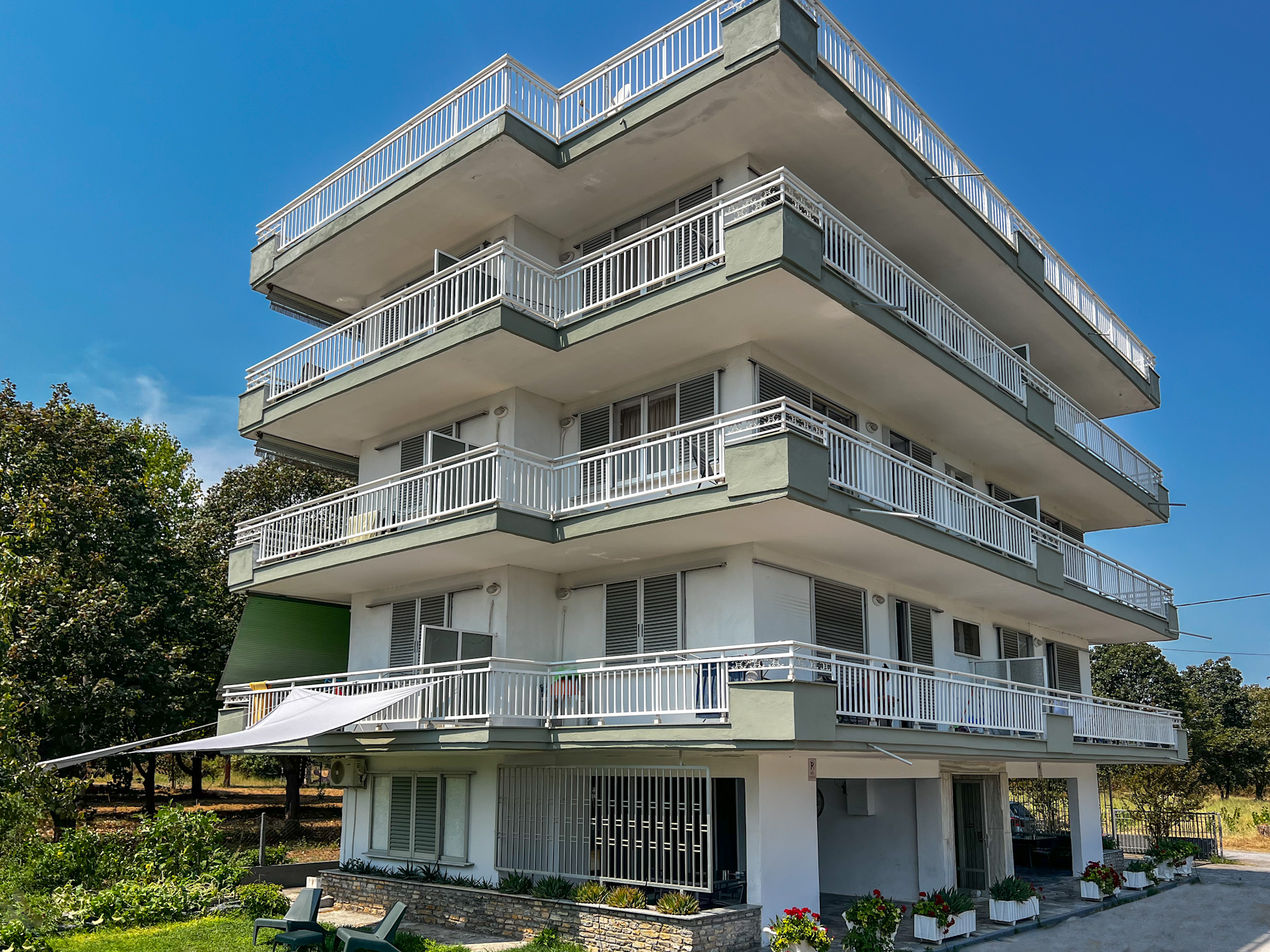 Exterior view of Prado Apartment Hotel, a multi-level building with spacious balconies overlooking lush green surroundings, showcasing modern architecture with a touch of nature.