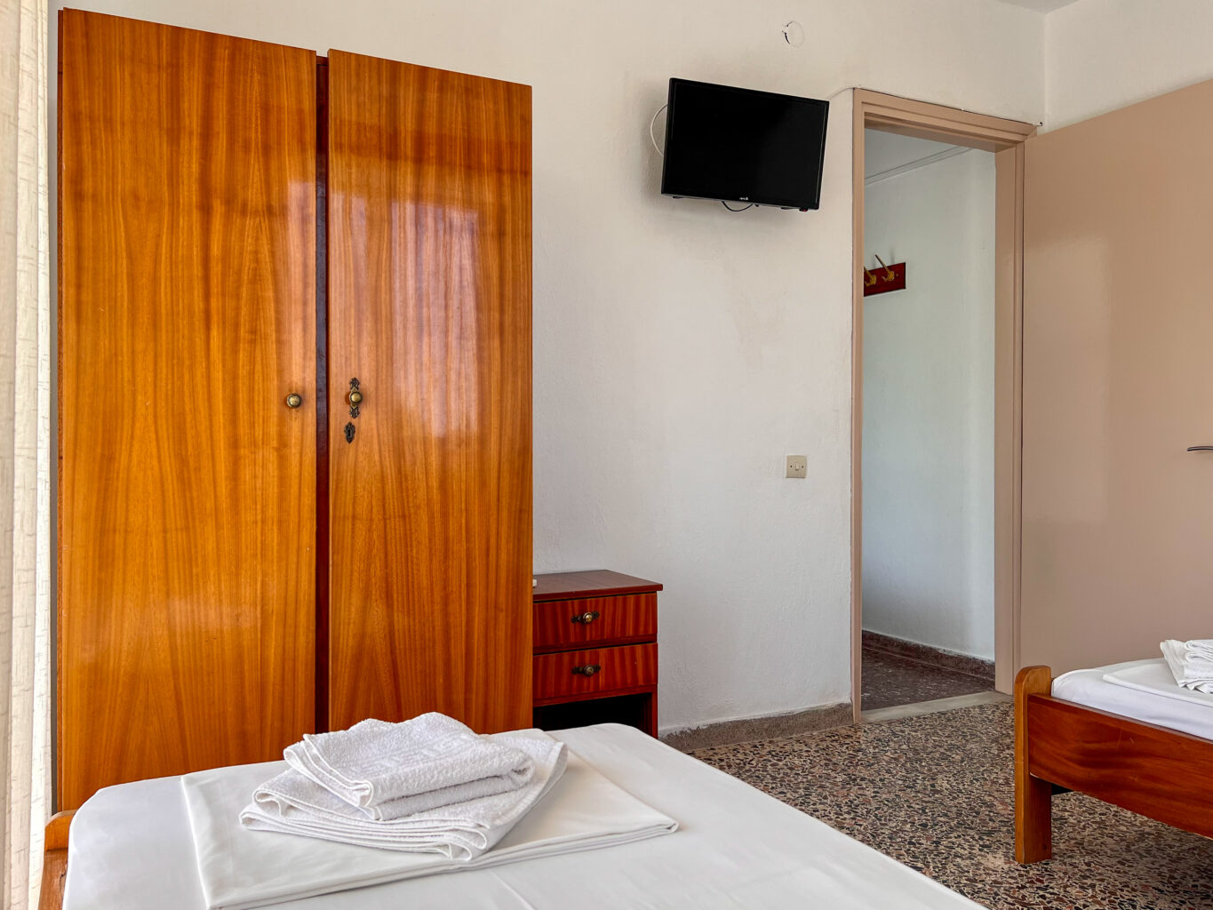 Hotel room with a wooden wardrobe, single beds, a small TV, and neatly folded towels