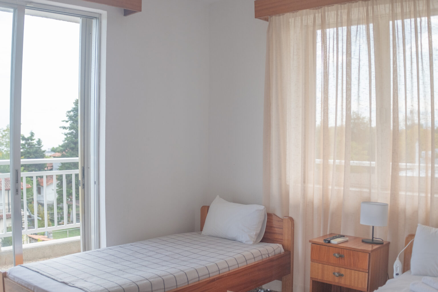 Interior view of a cozy single room at Prado Apartment Hotel, featuring a single bed with sheer curtains and a balcony view.