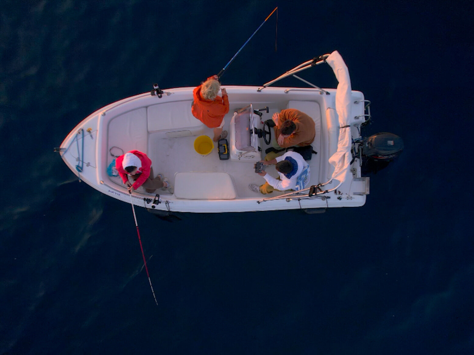 Aerial view of a small fishing boat with four people fishing in the deep blue waters of the Aegean Sea at dawn.