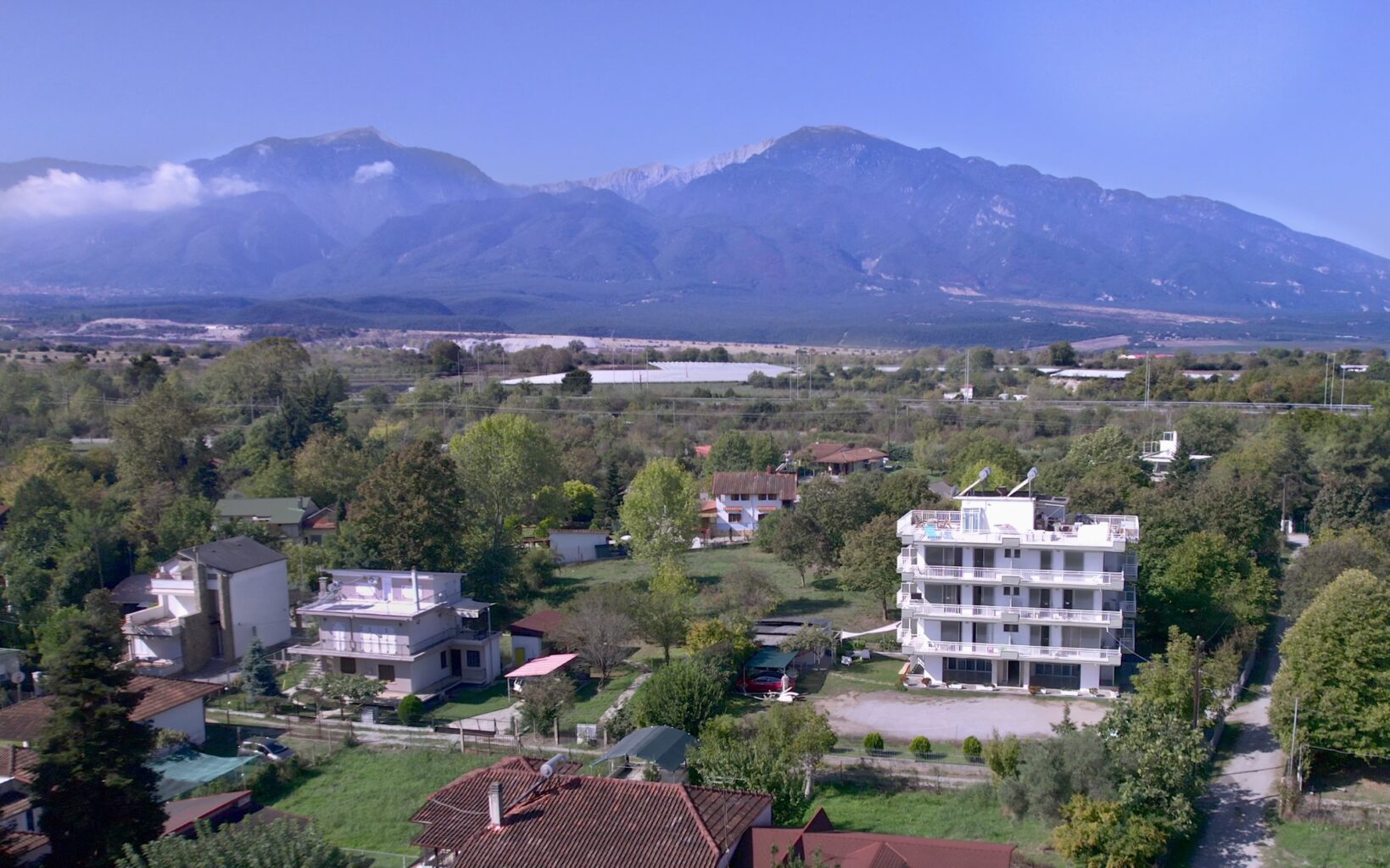 Aerial view of Prado Hotel in front of Mount Olympus, showcasing surrounding greenery and residential layout.