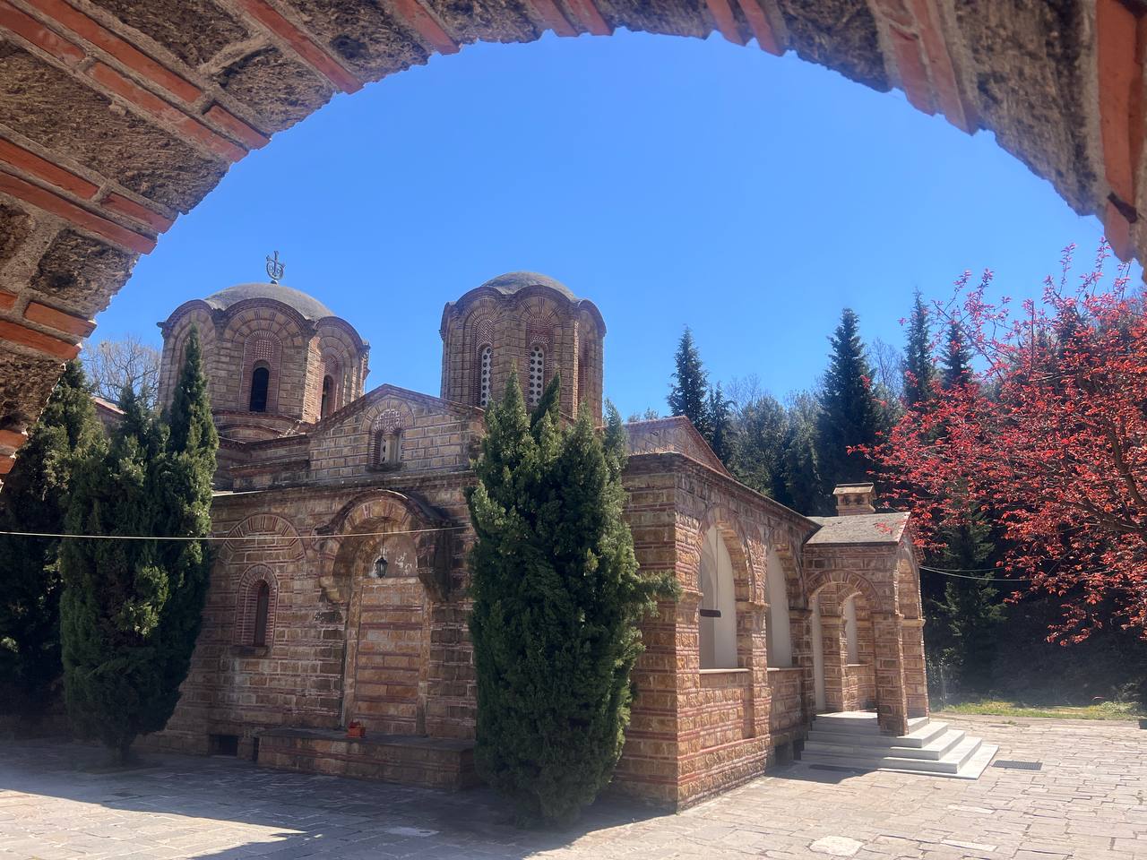 Byzantine church of Agios Dionysios Monastery on Mount Olympus seen through a stone arch, surrounded by cypress trees