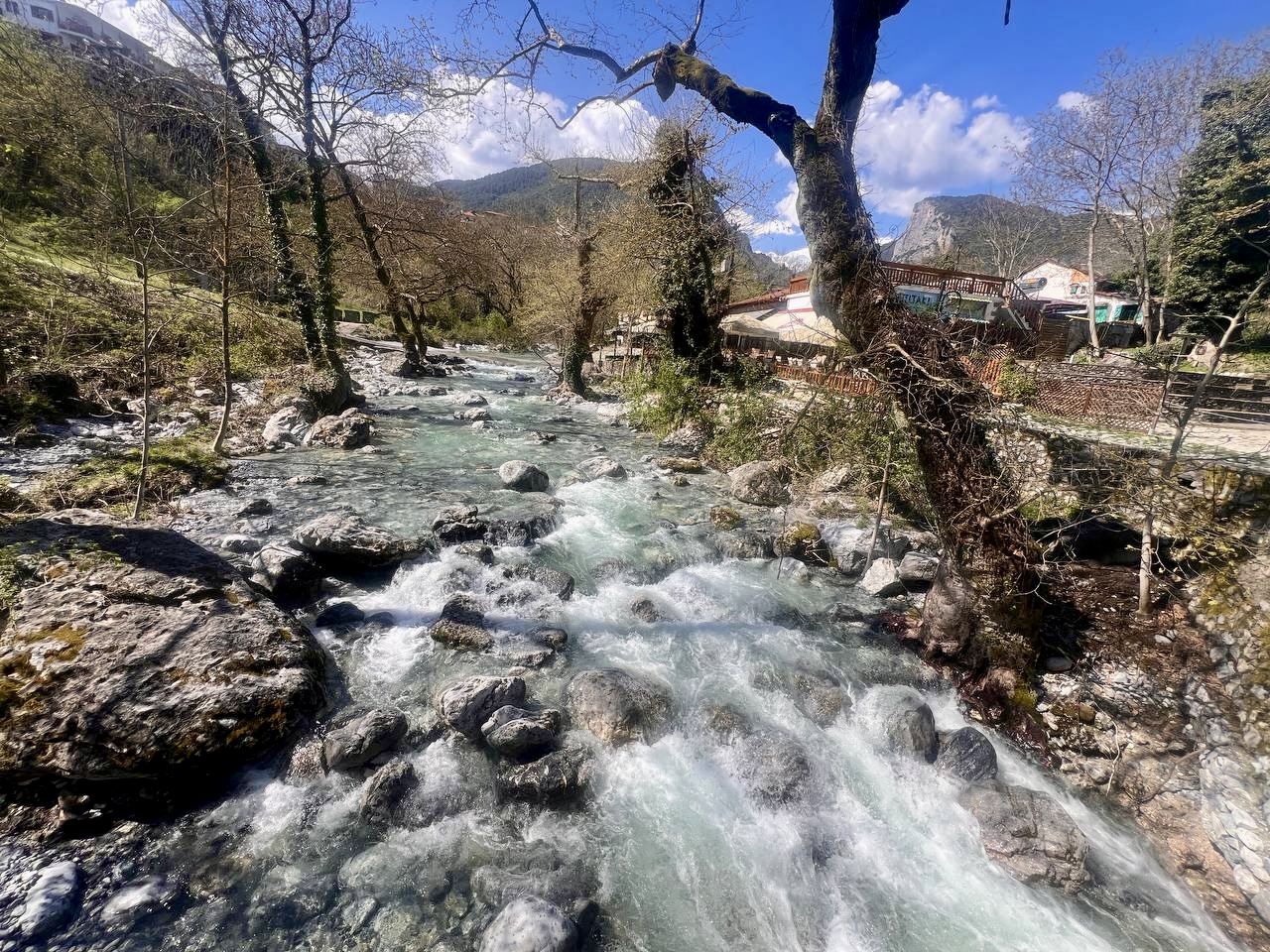 Enipeas river rushing through Litochoro town in spring with riverside cafes and Mount Olympus in the background